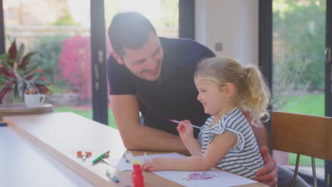 father and young daughter having fun at home sitting at table and painting decoration together - shot in slow motion