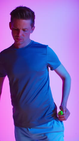 vertical video studio portrait of male tennis player with racket and ball against low key colourful mixed lighting 1