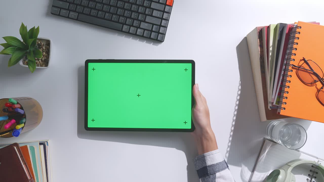 초록색 화면을 모방한 노트북 컴퓨터의 상단에서 아래로 볼 때, 펜, 안경, 그리고 물 한 잔을 가진 노트북 에 나무 사무실 책상 위에 크로마키 디스플레이가 있습니다.