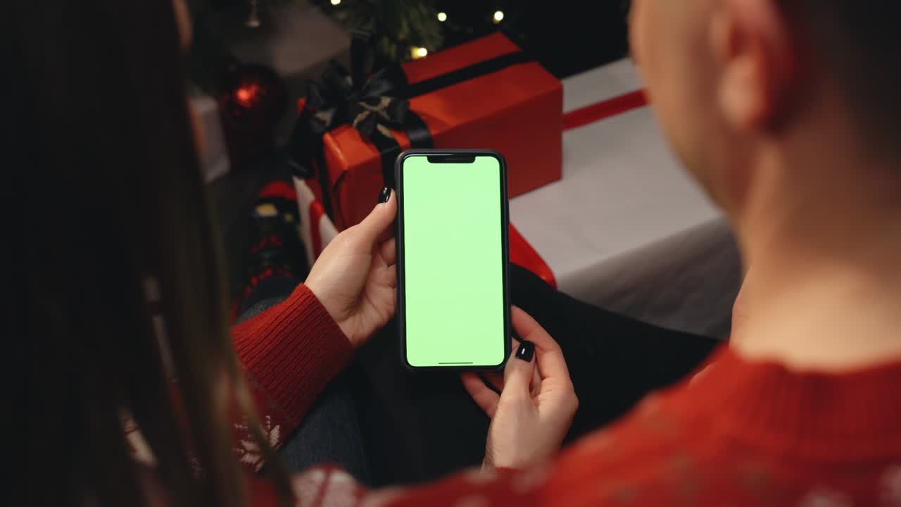 una pareja caucásica que usa un teléfono inteligente para una videoconferencia de navidad con una pantalla simulada verde. navidad, festividad y tecnología de comunicación