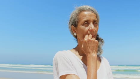 Vista-Frontal-De-Una-Mujer-Afroamericana-Senior-Activa-Y-Reflexiva-Con-La-Mano-En-La-Barbilla-Parada-En-La-Playa-4k