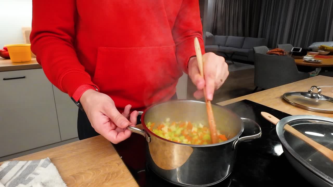 A person in a red sweater stirs a pot of vibrant vegetables on a modern stovetop. The cozy kitchen setting enhances the warm, inviting atmosphere of home-cooked meals