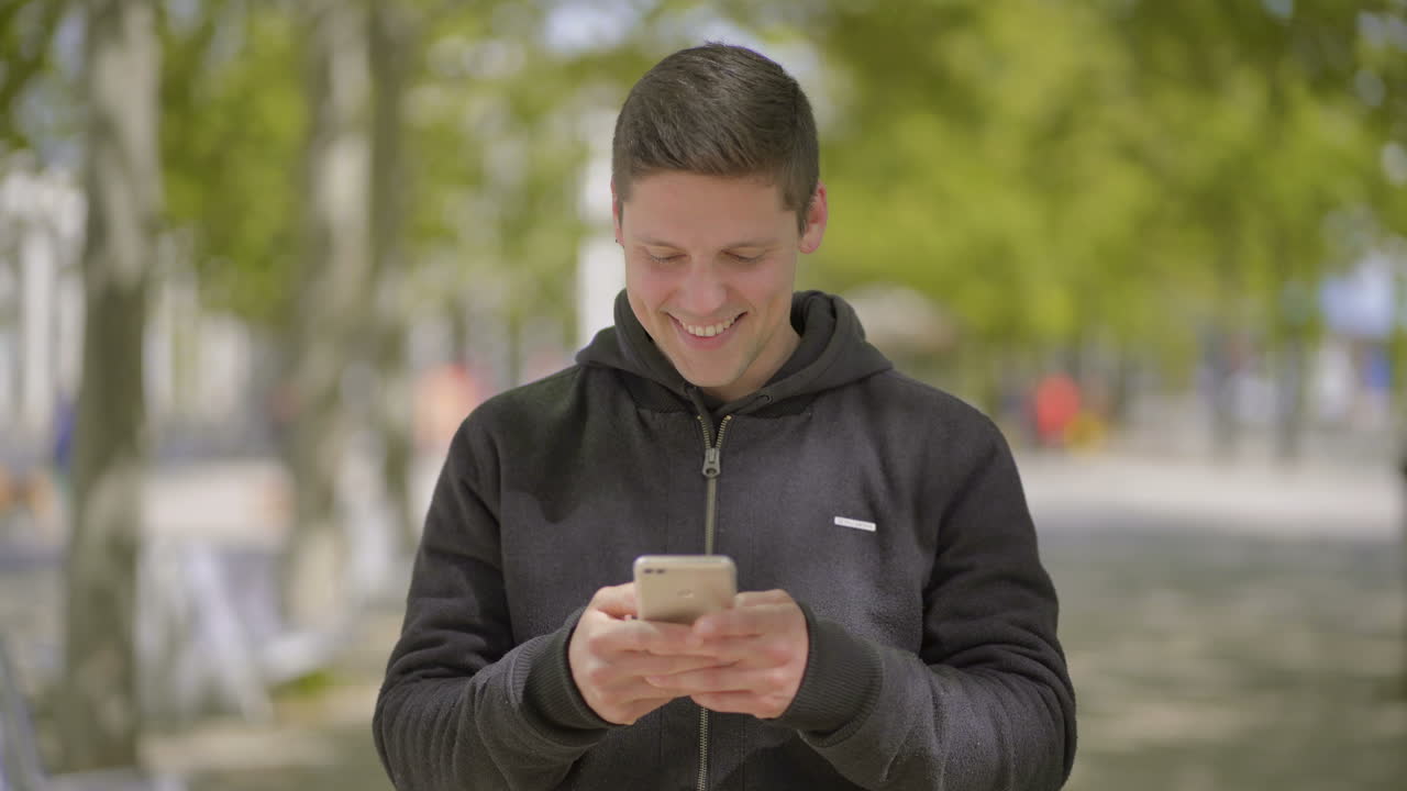 밖에서 휴대폰을 사용하는 미소 짓는 젊은 남자