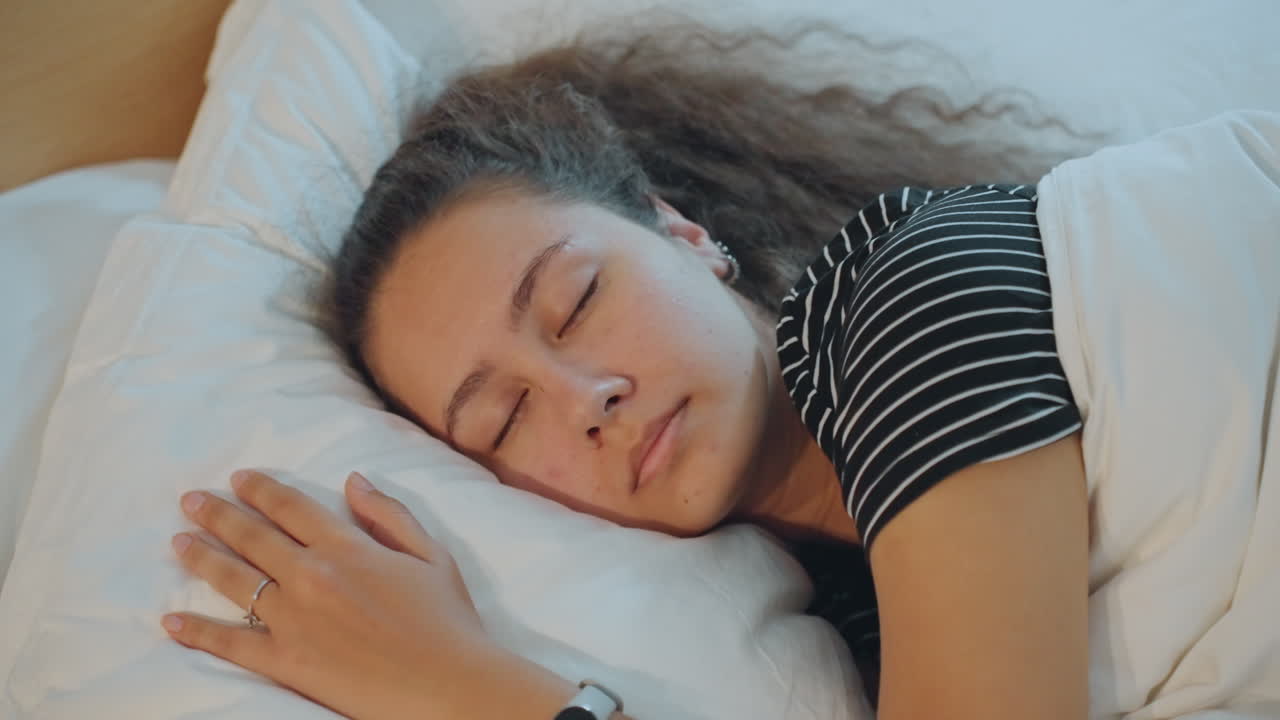 Fredelig person i hotelseng. Rolig gæst hviler komfortabelt med sagte vejrtrækning på hotelværelset. Fredfyldt rejsende nyder hvilefuld søvn og rolig atmosfære efter en rejse eller et ophold.