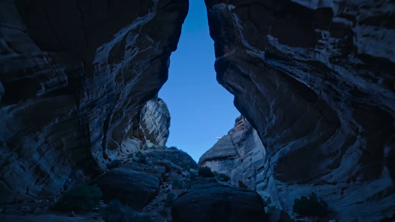 Inquadratura inclinata della fotocamera che rivela un alto arco triangolare in un canyon, mostrando cielo blu, strati di arenaria e massi.