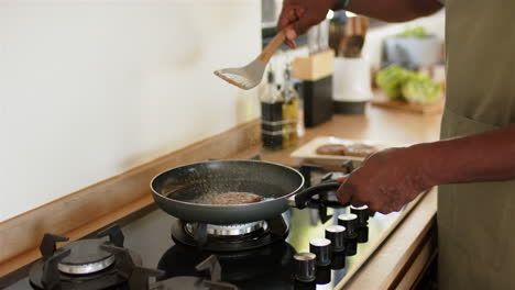 cooking burger patties on stovetop, person using spatula in modern kitchen