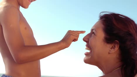 smiling son applying sunscreen on his mothers nose