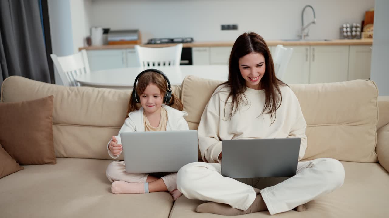 Mother and her cute little girl using laptops sitting next to each other on couch