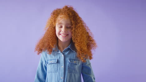 studio shot of smiling girl with red hair jumping into bottom of frame against purple background