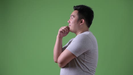 young handsome overweight asian man against green background