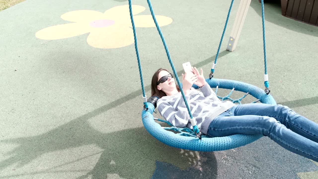 la mujer está balanceándose en un columpio vacío y hablando por video chat en el teléfono móvil.