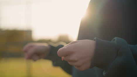 초록색 옷을 입은 여자의 클로즈업은 초록색과 건물을 보여주는 흐릿한 배경으로 손목을 회전시켜 야외 환경에서 손의 움직임을 강조하고 초점을 맞추고 있습니다.
