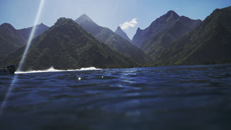 sunlight shines on ocean water surface as waves break looking into tropical green mountain valleys