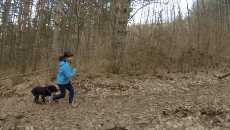 Girl-running-in-mountain-trail-in-forest-with-black-dog,-autumn-time