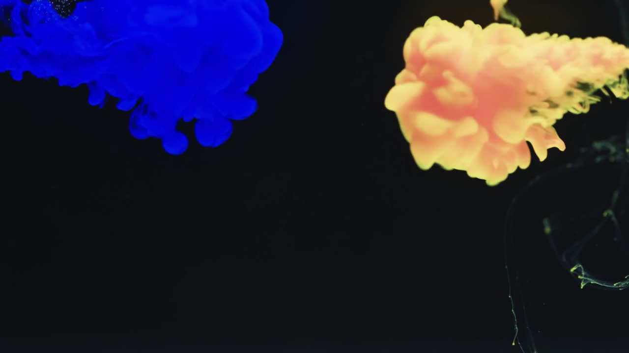 Slow motion video of blue and yellow watercolor ink mixing in water against black background