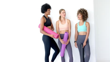 three women are standing together, holding yoga mats