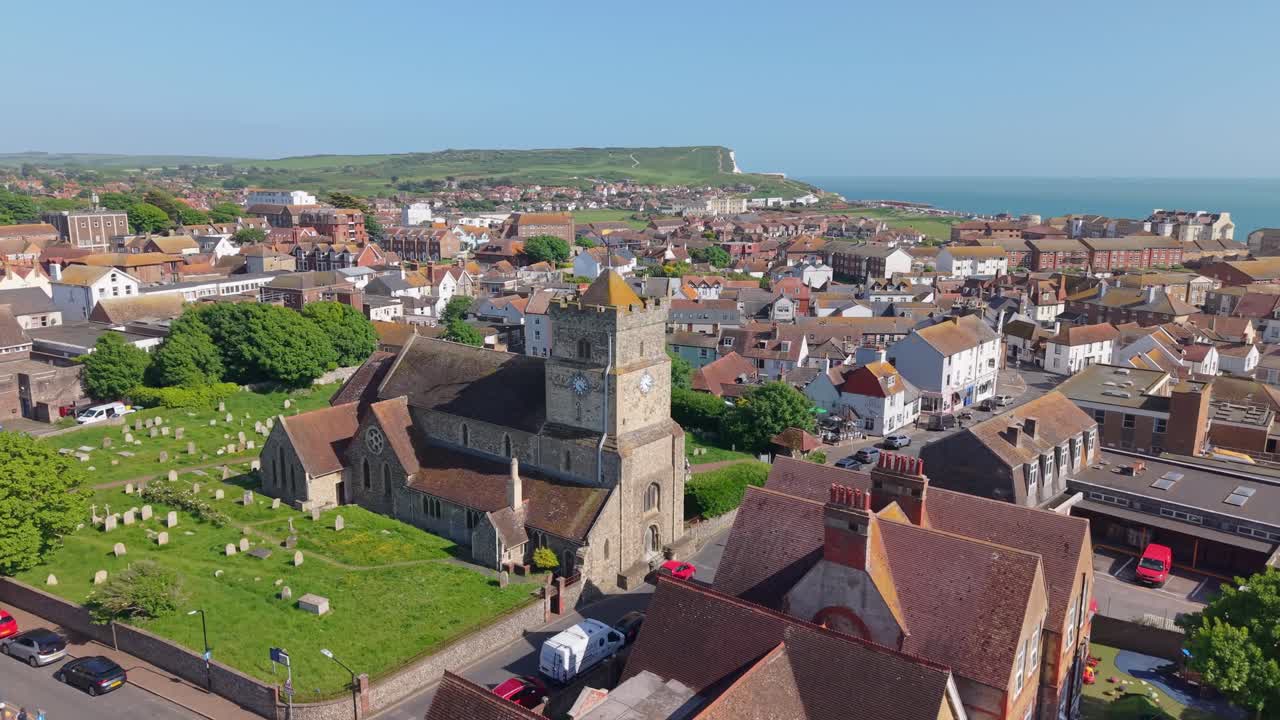 Drone orbit around St. Leonard's Church in Seaford, capturing the historic stone architecture, the surrounding green hills, and the stunning English Channel coastline