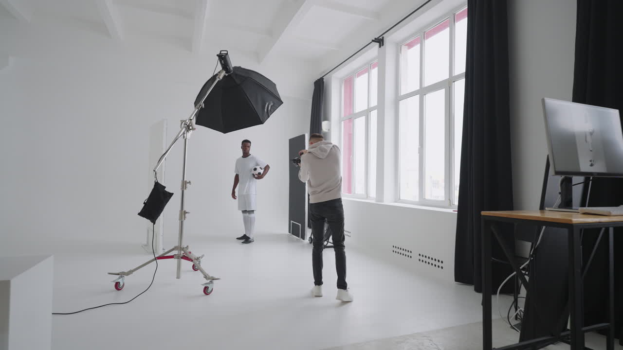 무대 뒤의 사진 촬영: 사진 스튜디오의 사진 작가가 흑인 프로 축구 선수의 사진을 찍기 위해 플래시를 사용합니다. 스포츠 잡지 광고 스튜디오의 사진 촬영