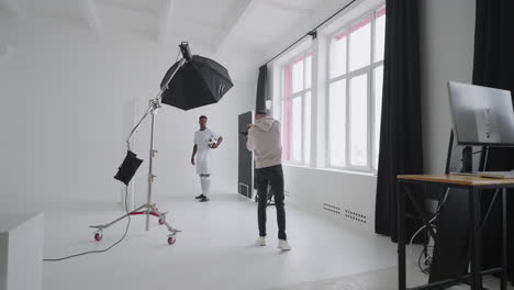sesión de fotos detrás de las cámaras: un fotógrafo en un estudio fotográfico utiliza un flash para fotos de un jugador de fútbol profesional negro. sesión de fotos en el estudio de una revista deportiva de publicidad