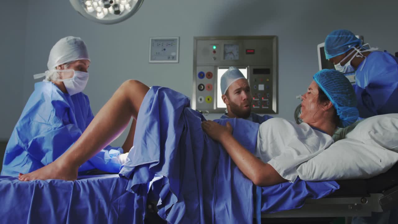 vista lateral de una cirujana caucásica examinando a una mujer embarazada durante el parto en el teatro de operaciones en