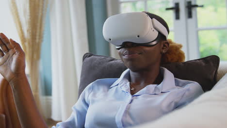 woman relaxing lying on sofa at home wearing vr headset and interacting with ar technology