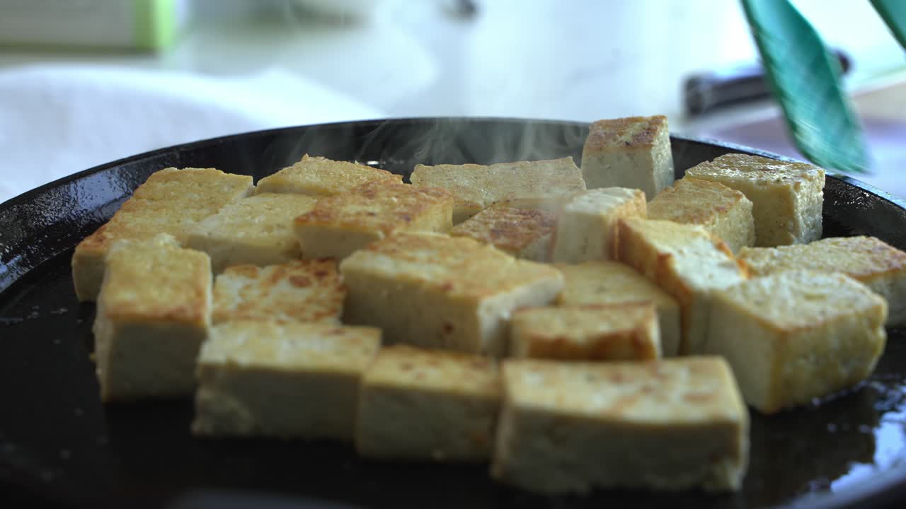 Primo piano del vapore che esce dal tofu in cottura in padella. Ingredienti speciali per cucinare un pasto: due lattine di fagioli, riso, platano, avocado, cipolla rossa e coriandolo.