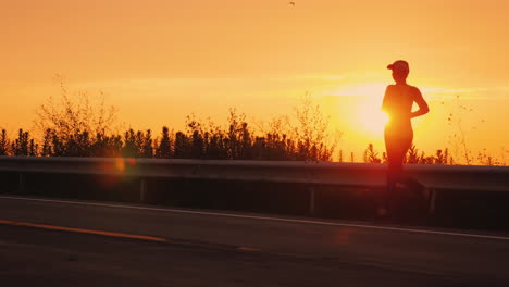 active and healthy lifestyle - woman silhouette running along the road along the sea at sunset