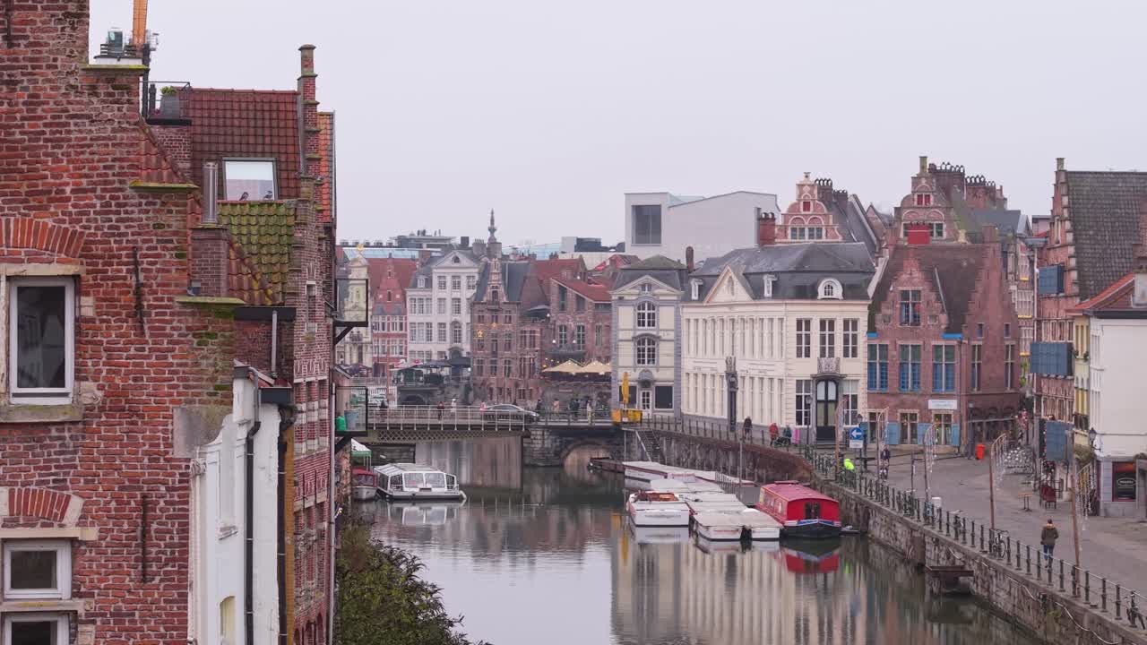 Una vista sul lungocanale di Gand in una giornata nuvolosa, con bellissime case storiche, riflessi calmi e un'atmosfera urbana pacifica.