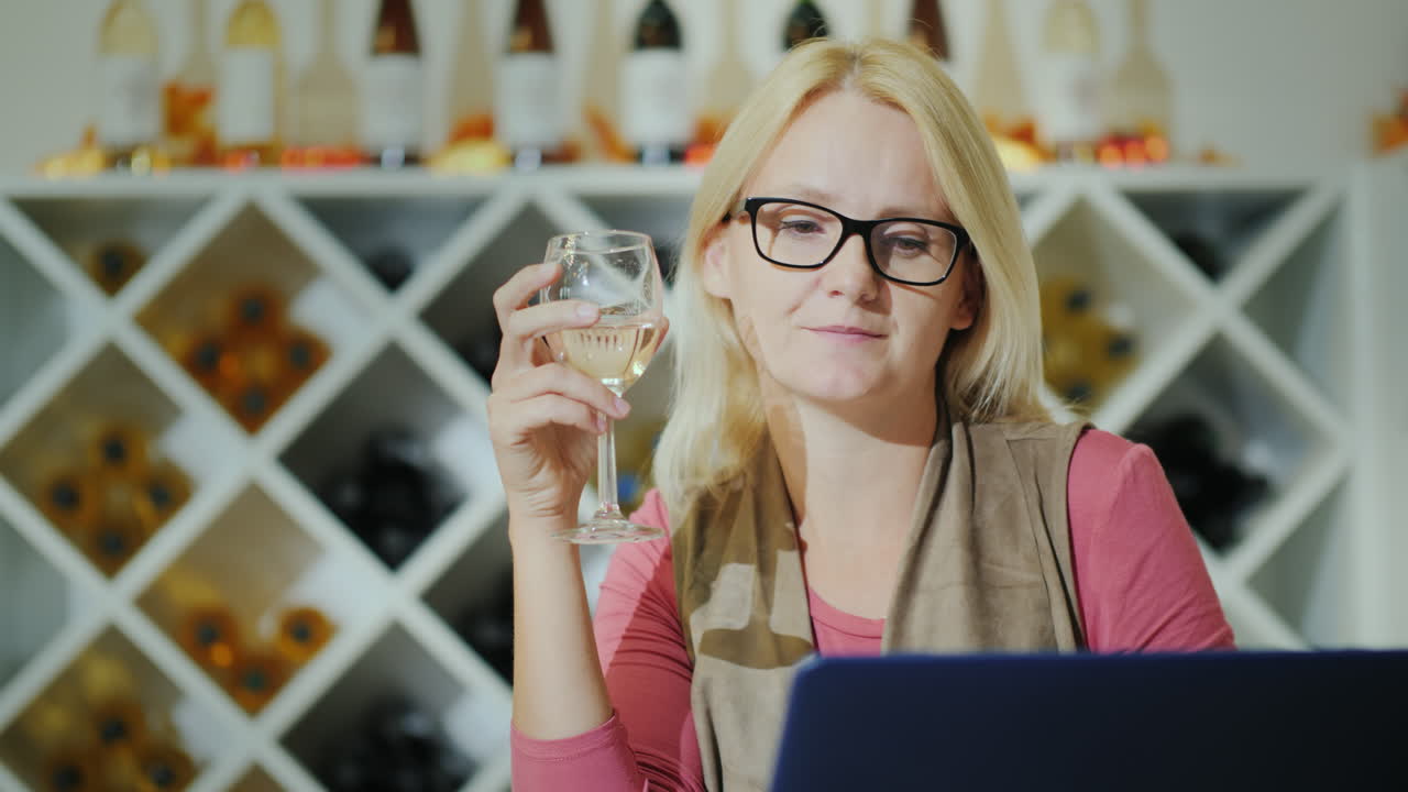 mujer catando vino sentada en una mesa en una bodega usando una laptop