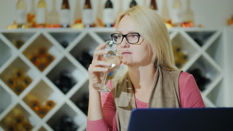 mujer catando vino sentada en una mesa en una bodega usando una laptop