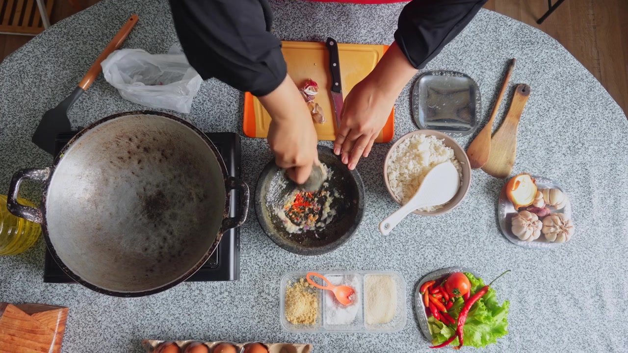 Ovenfra-perspektiv av en kokk som maler chilifrukter og aromatiske urter ved hjelp av en steinmorter for å lage krydderpasta