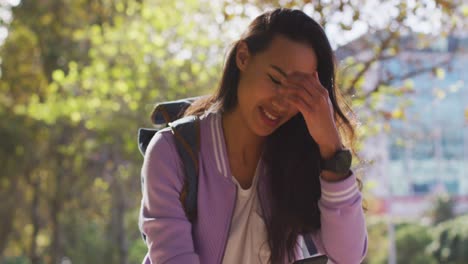 Mujer-Asiática-Sonriendo-Mientras-Usa-Un-Teléfono-Inteligente-Sentado-En-El-Parque