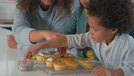 close up of mother and children in kitchen decorating cupcakes together