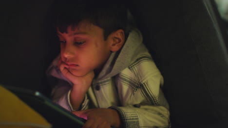 close up of young boy in home made camp made from cushions playing with digital tablet at night 2