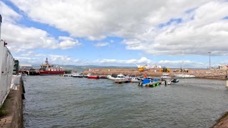 wide shot of small boats moving into cromarty harbor, with colorful waterfront houses and dramatic clouds. natural daylight, steady camera, calm maritime atmosphere