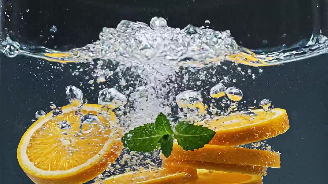 Fresh orange slices and mint leaves splashing into clear water