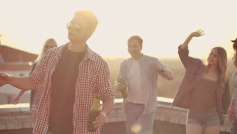 a young boy in trendy glasses with beer moves in a dance at a party with his friends on the roof.