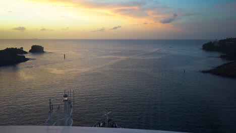 Vista-Panorámica-Desde-El-Tablero-De-Un-Crucero-Que-Navega-Por-El-Tranquilo-Mar-Caribe-Por-La-Noche,-Puesta-De-Sol-Dorada-En-La-Distancia-A-La-Izquierda,-Acantilados-Y-Boyas-En-Ambos-Lados,-Toma-Panorámica-Estática-De-Fhd