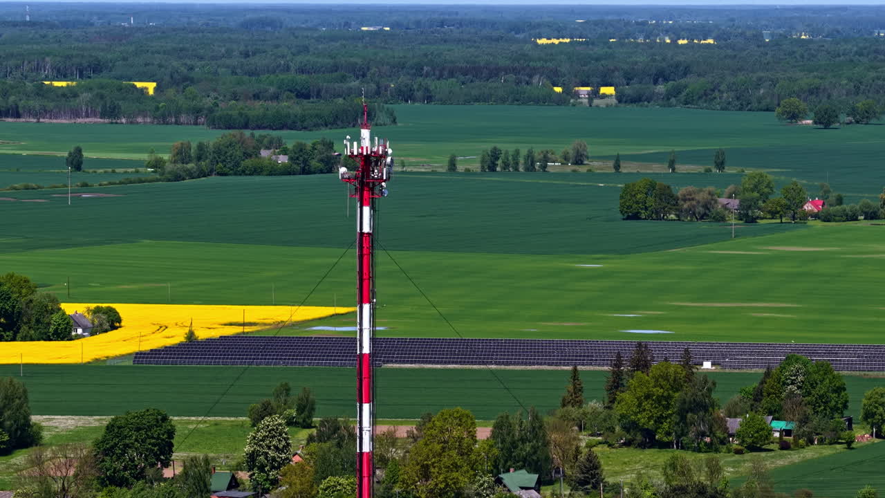 Cell tower in green fields, with solar panels and yellow rapeseed fields nearby