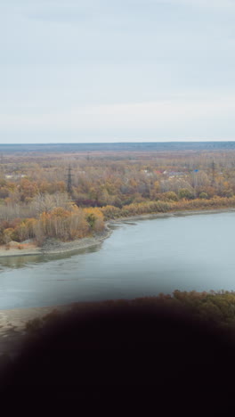 vista panorámica de la naturaleza con árboles de otoño coloridos a lo largo de una orilla del río, follaje de otoño vibrante que se refleja en un río pacífico, con vistas lejanas de paisajes ondulados bajo un cielo nublado