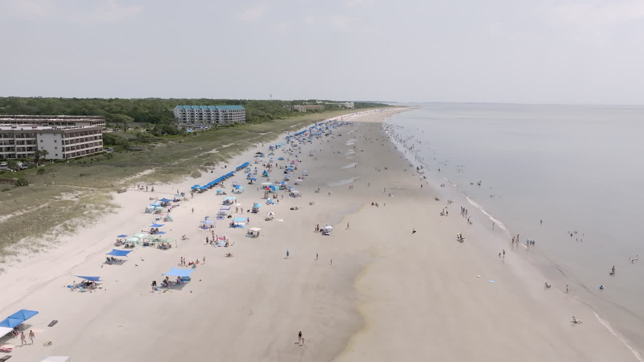 Long aerial view of Hilton Head beach lined with umbrellas and resort buildings, stretching into the hazy horizon