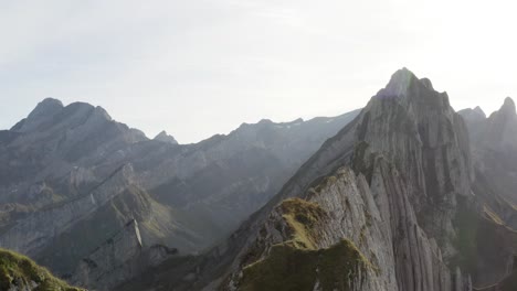 Aerial-flying-backwards-revealing-a-person-enjoying-the-view-of-Schäfler-mountains,-Appenzell,-Switzerland