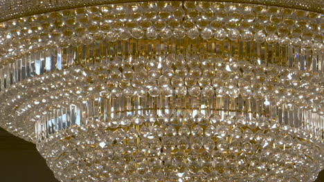 Close-up-dolly-shot-of-a-spectacular-gold-and-crystal-light-chandelier,-the-extravagant-and-glamorous-decor-of-the-beautiful-wedding-venue-the-Excellency,-Midlands,-England