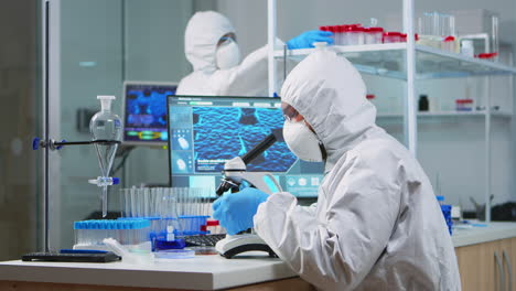 chemist researcher in coverall looking at bacteria sample from glass