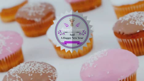 Animation-of-christmas-greetings-on-tag-over-cupcakes-on-white-background