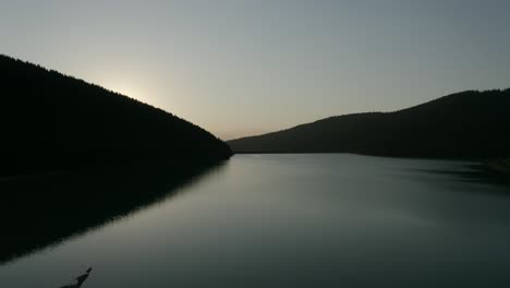 Sunset-behind-the-dark-mountain-forests-of-Frumoasa-Dam,-Romania--Aerial