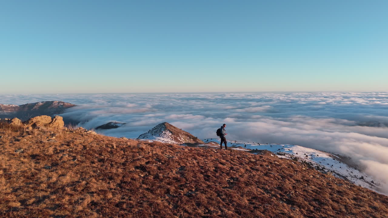 Escursionista sopra le nuvole all'alba su una cima montuosa, provando libertà e avventura.