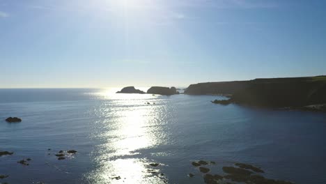 Vista-Aérea-Del-Sol-Reflejándose-En-El-Océano-Atlántico-Y-La-Costa-Rocosa-A-Lo-Largo-De-La-Costa-De-Cobre-De-Waterford-En-El-Sur-De-Irlanda.