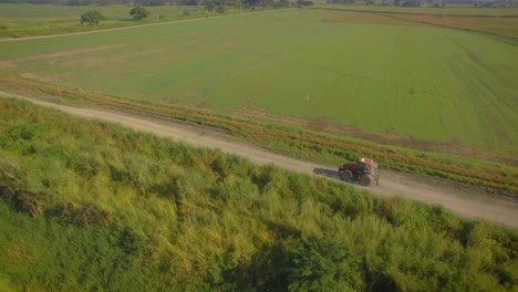 aerial shot of a tractor going on a dirt road across the countryside