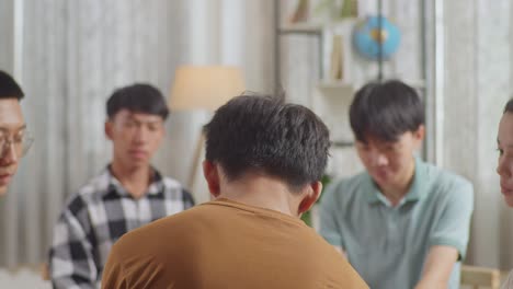 close up of asian teen group sitting in chairs forming a circle discussing at home. teen students support a boy in brown t-shirt not to crying